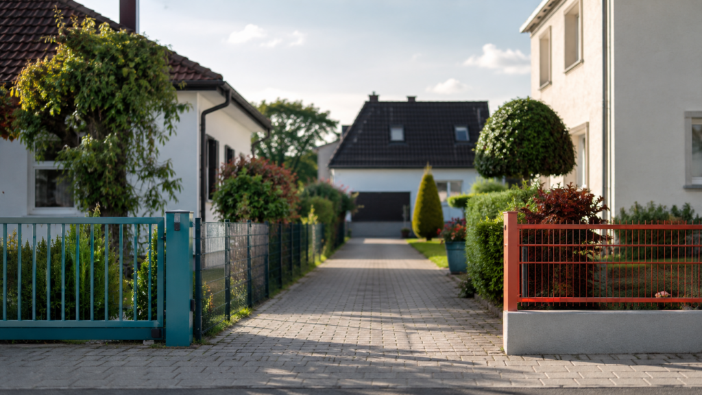 Private Zufahrtsstraße zwischen zwei Wohnhäusern mit Gartenzäunen und Hecken als Symbol für Wegerecht und Grundstückszugang